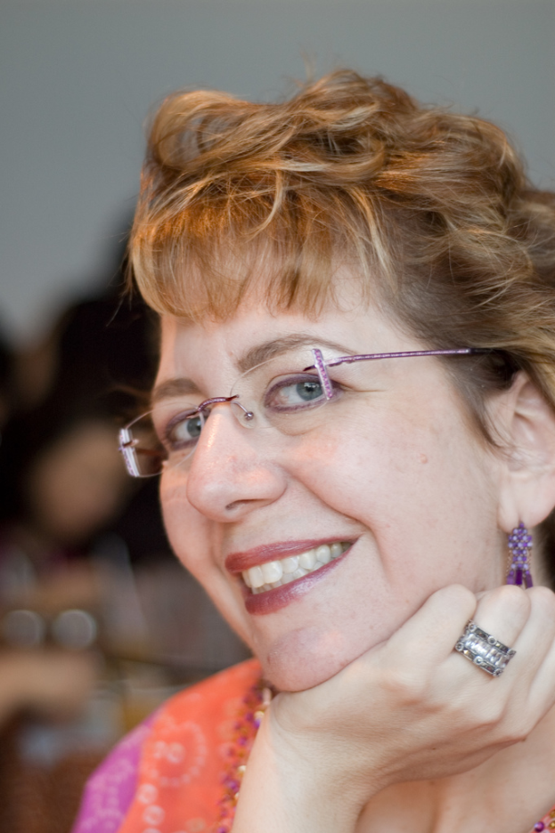 Eine Frau mit Brille lächelt, mit einem unscharfen Hintergrund.