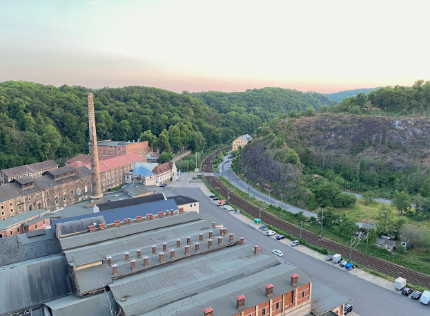 Luftaufnahme einer Stadt mit dichtem Gebäudebestand, befahrenen Straßen, Strommasten, verstreuten Bäumen, fernen Hügeln und einem bewölkten Himmel, der auf ein Kohlebergbaugebiet hinweist.