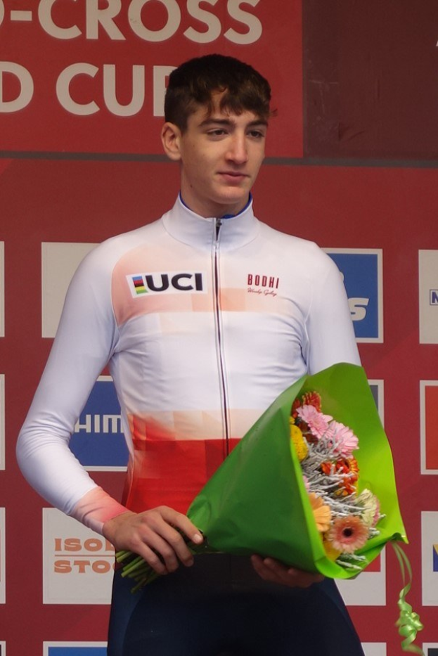 Ein Mann steht selbstbewusst auf einem Podium und hält einen Blumenstrauß, feiert einen Sieg mit einem fröhlichen Ausdruck.