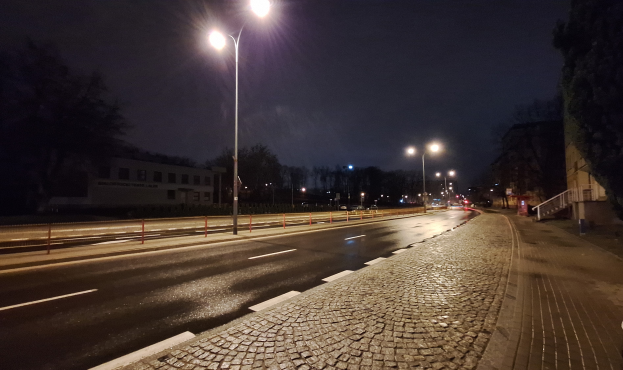 Eine nächtliche Straßenansicht mit Straßenlaternen, die die Straße, Gehwege, Geländer, Bäume, Gebäude und andere Gegenstände beleuchten.