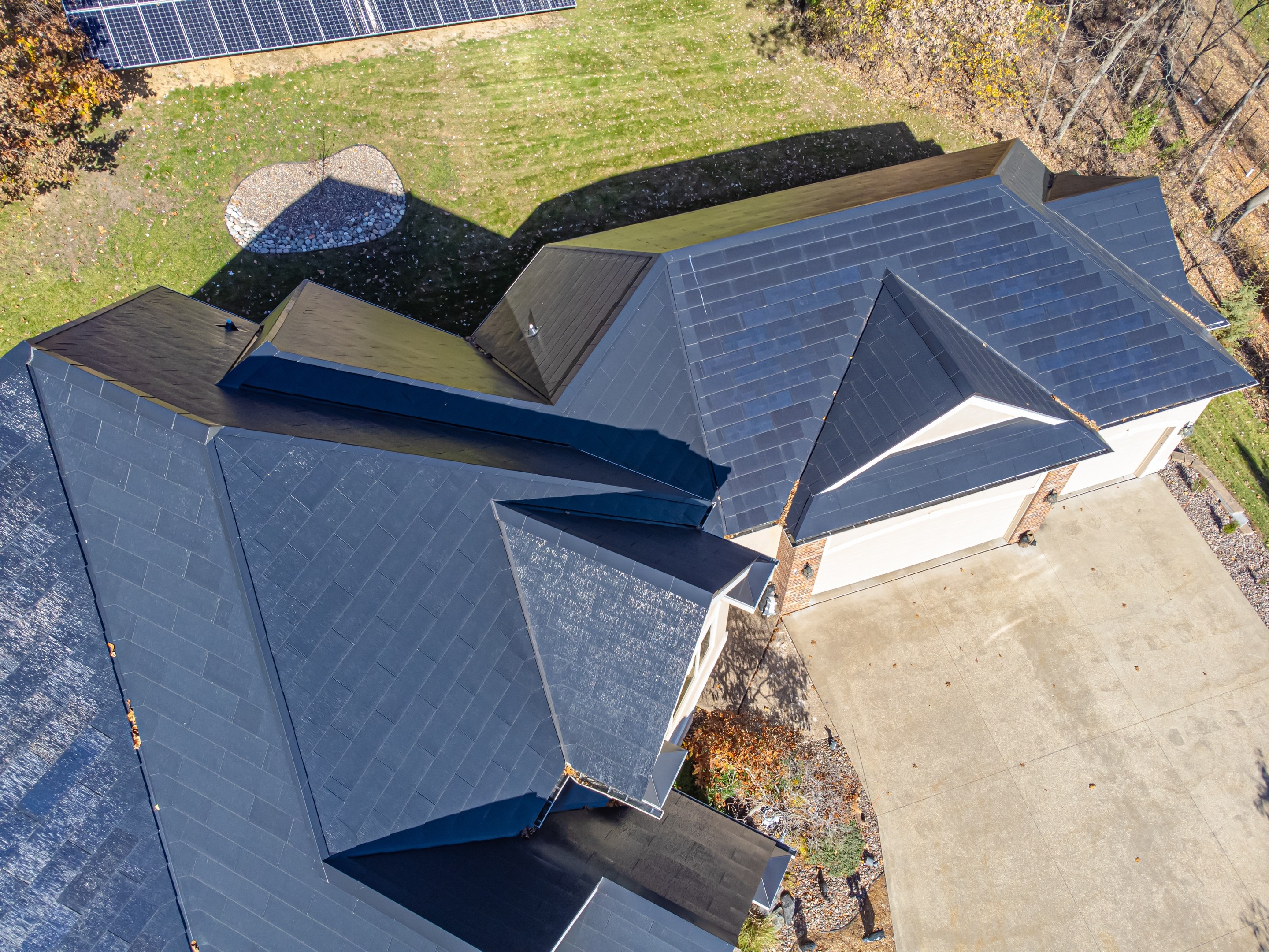 Luftaufnahme eines Hauses mit in das Dach integrierten Solarpanelen, umgeben von Bäumen, Gras und einem Zaun.