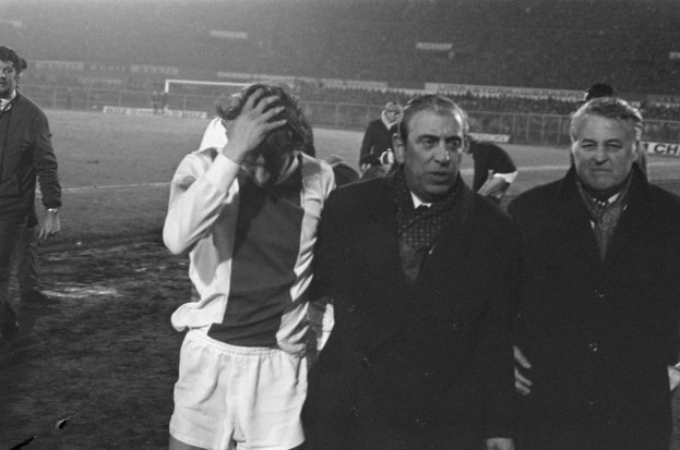 Schwarzes und weißes Bild von Männern auf einem Fußballfeld in scheinbarer Feierlaune, mit einem Stadion im Hintergrund.