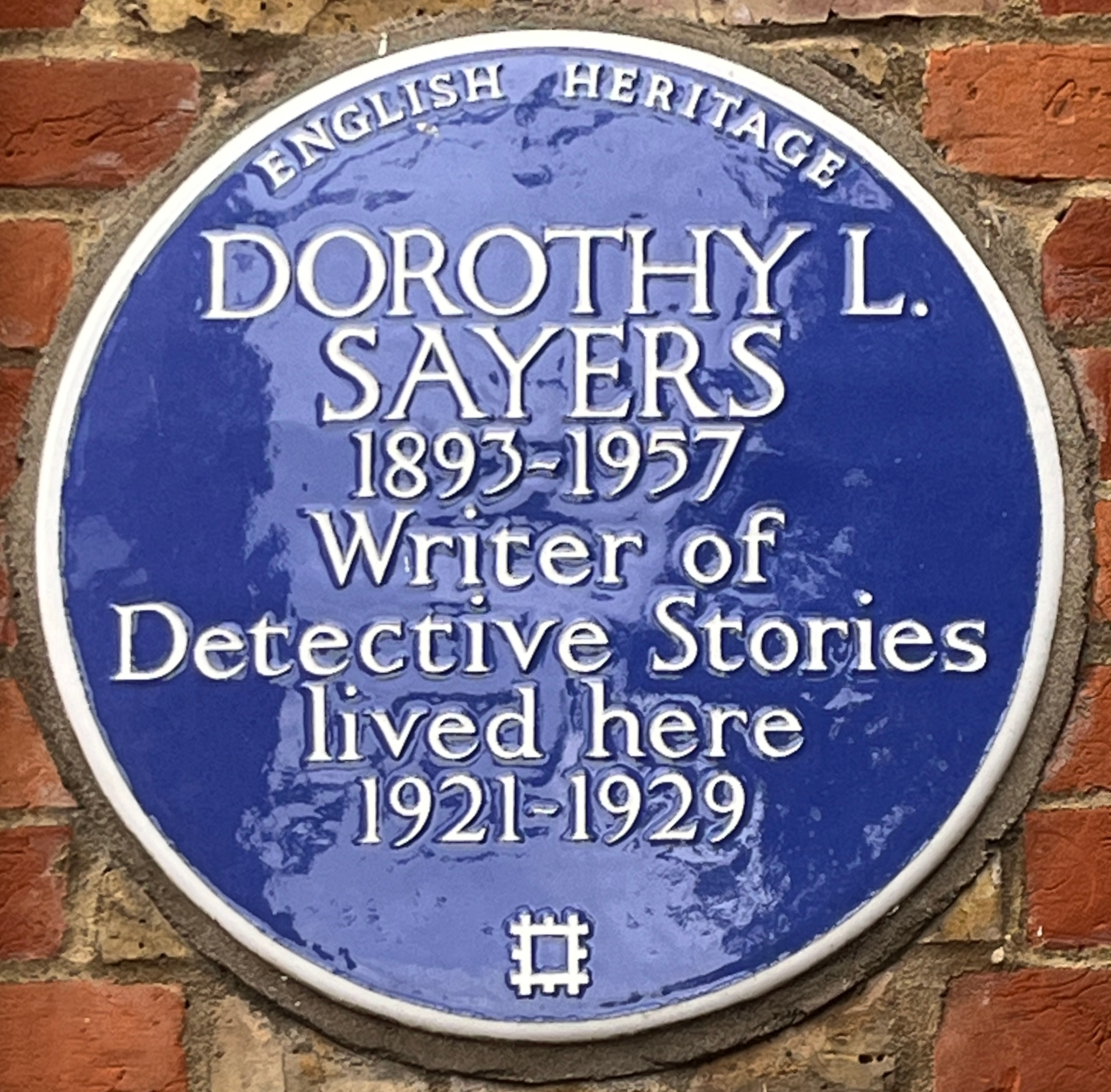 Ein rundes blaues Schild an einem Backsteingebäude mit der Inschrift "Dorothy L. Sayers"