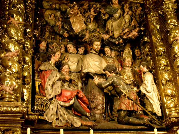 Eine Gruppe von detailreich gestalteten Statuen in einer Kirche, umgeben von brennenden Kerzen mit hellen Flammen, die eine warme und einladende Atmosphäre schaffen.