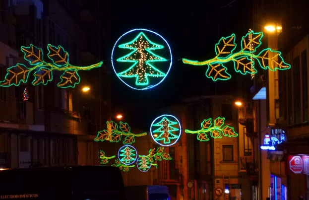 Straße in der Stadt mit festlichen Weihnachtslichtern geschmückt, die Blätter und andere Schmuckstücke zeigen, mit fahrenden Fahrzeugen und Gebäuden auf beiden Seiten.