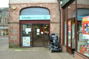 Eine Apotheke mit einem vor dem Gebäude geparkten Fahrzeug und einem Gebäude in der linken Ecke.