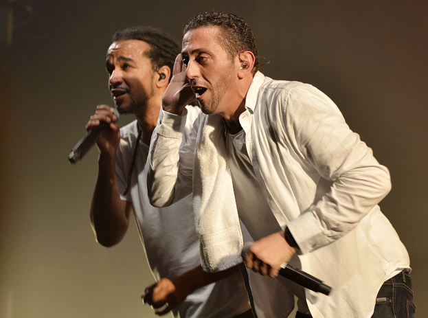 Zwei Männer in legerer Kleidung auf der Bühne, jeder hält ein Mikrofon in der Hand.