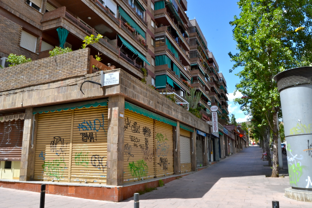 Eine Szene mit mehreren Gebäuden mit Fenstern, grünen Kleidungsstücken, Geschäften, Schildern und umgebenden Bäumen und Pflanzen.