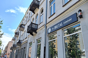 Eine Straßenansicht eines Barbiers in Berlin, Deutschland, mit Gebäuden, die Fenster, Geländer, Balkone und Namensschilder, Bäume, Laternen und Menschen auf der Straße unter einem bewölkten Himmel zeigen.