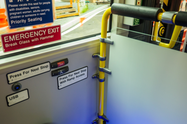 Notausgangsschild an der Seite eines Zugs, mit Tür, Griff und Glasfenster, das äußere Elemente zeigt.