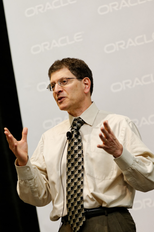 Eine Person steht vor einer Sponsorentafel und tr├Ągt Kleidung und Brille.