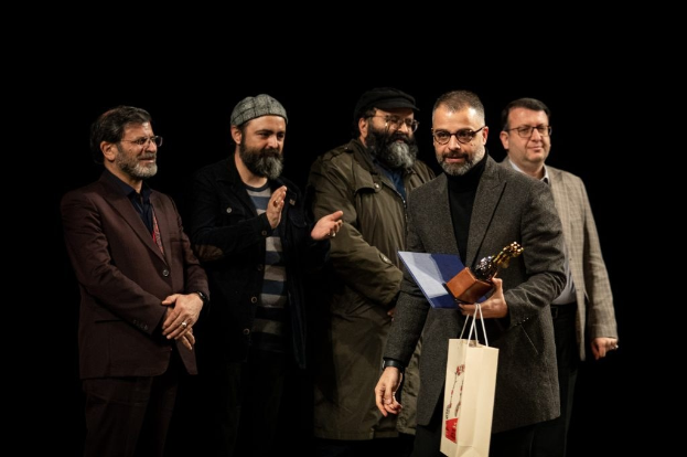 Eine Gruppe von Männern auf einer Bühne, einer hält eine Tasche und eine Trophäe, feiernd bei der Eröffnungsnacht des Berliner Filmfestivals.
