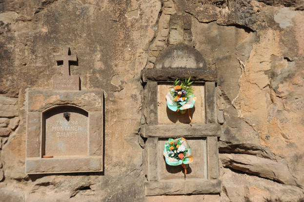 Memorials carved on a wall with flower bouquets placed in front of them.