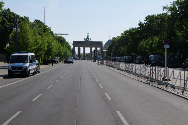 Ein Polizeiwagen steht auf der Seite einer vielbefahrenen Straße vor dem Reichstagsgebäude in Berlin, Deutschland, mit Barrieren, Schildern, Bäumen und Laternen im Hintergrund und einer bewölkten Himmel.