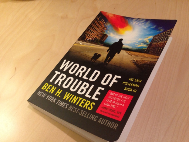 Ein Buch mit dem Titel 'World Of Trouble' mit einem Bild eines Mannes und eines Hundes auf einem Tisch.
