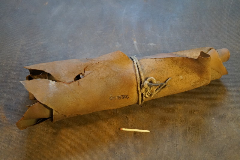 Eine braune Papiertüte in Form einer Granate mit Henkel, verschnürt mit einem Seil und eine Zigarette daneben auf einem Tisch.