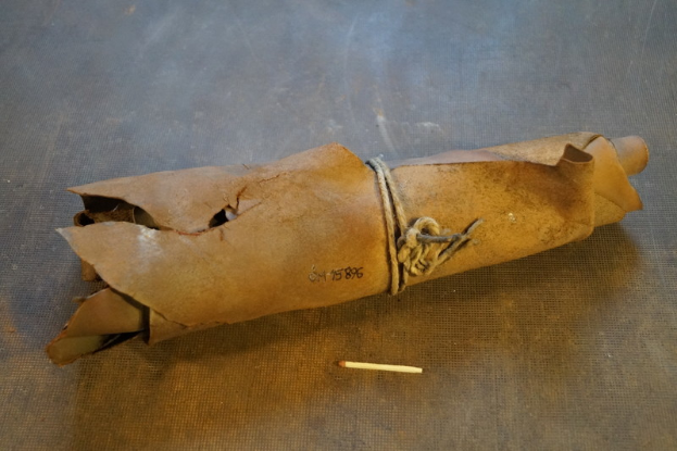 Eine braune Papiertüte in Form einer Granate mit Henkel, verschnürt mit einem Seil und eine Zigarette daneben auf einem Tisch.