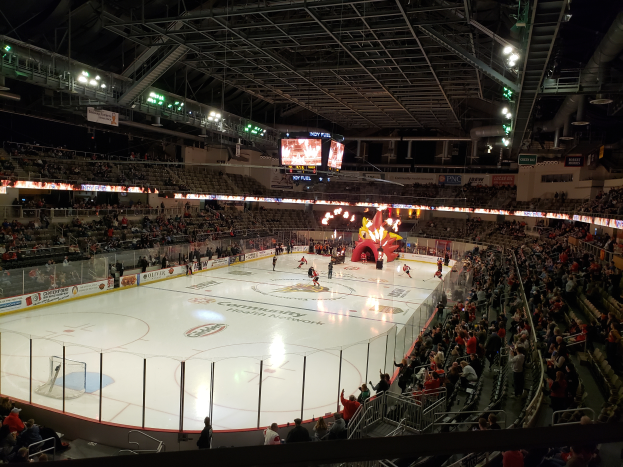 Ein Hockey-Spiel im Columbus Blue Jackets Stadion mit Zuschauern auf Sitzen und Stehplätzen, umgeben von einem Zaun und Bannern, unter einem Dach mit Metallstangen, Lampen und zwei Bildschirmen.