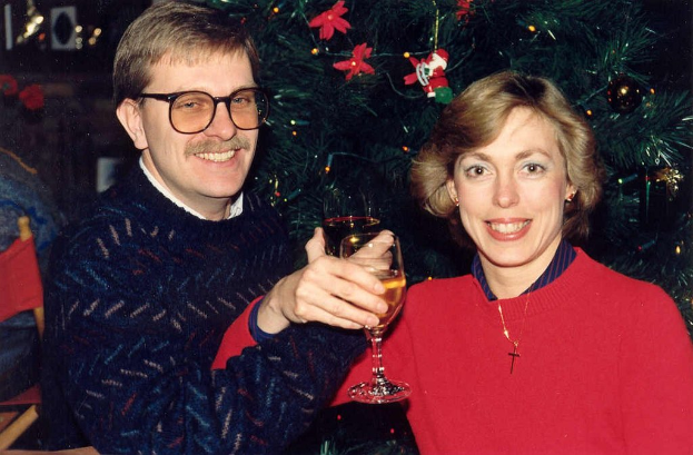 Ein Paar lächelt mit Weingläsern in der Hand vor einem Weihnachtsbaum