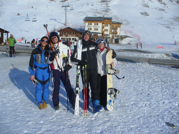 Vier Personen posen für ein Foto mit Skatereinlagen und Werkzeugen, mit Gebäuden und anderen Menschen im Hintergrund, alles vor einer schneebedeckten, eisigen Berglandschaft.
