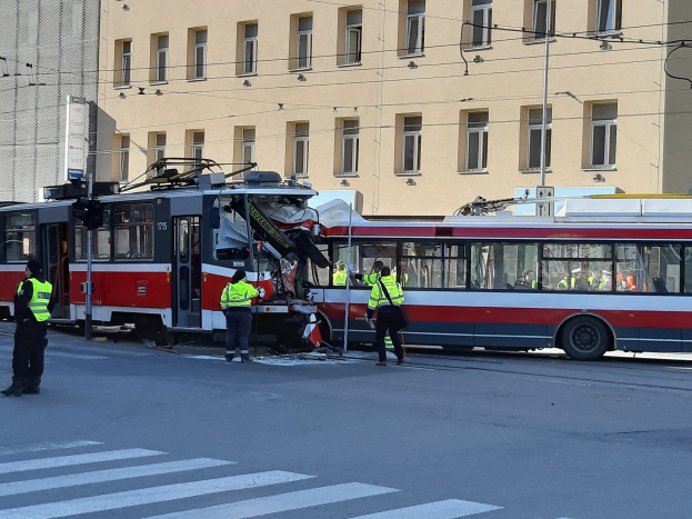 Rote und weiße Tram ist auf der Straße zum Stehen gekommen und hat ein paar Menschen in der Nähe und ein Gebäude im Hintergrund.