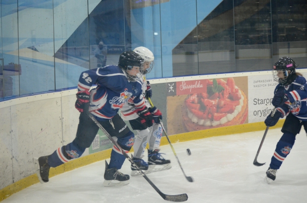 Gruppe junger Menschen, die Eis-hockey auf einer Indoor-Eisfläche spielen, mit Helmen, Sportuniformen und Schlittschuhen, während sie Hockey-Schläger halten, mit einem Plakat im Hintergrund auf einer Glaswand.