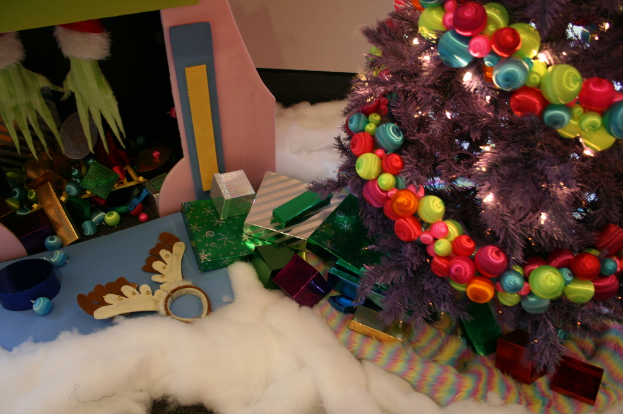 Drinnen, ein geschmückter Weihnachtsbaum auf der rechten Seite, Geschenkboxen und Dekorationen in der Mitte, eine Hütte mit Dekorationen oben links und Baumwolle und Wolle unten.