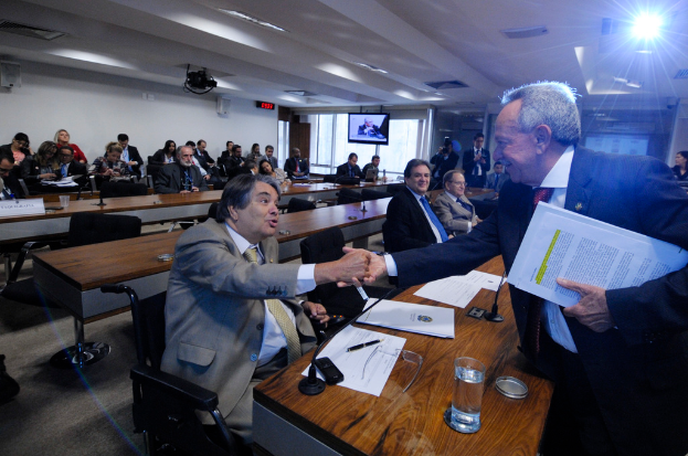 Eine Gruppe von Menschen ist in ein Gespräch vertieft und sitzt in einem Raum mit anderen im Hintergrund, unter einer Decke mit Beleuchtungskörpern.