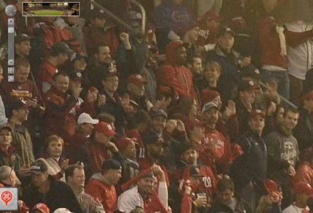 Eine Menschenmenge mit Gegenständen in den Händen, animierte Logos oben links und unten links sowie ein Stadionbild oben.