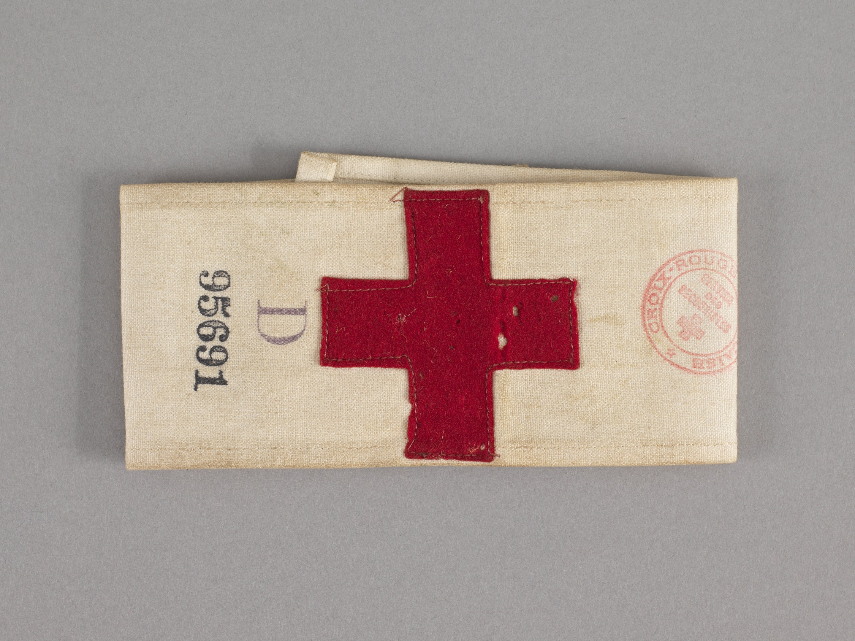 Ein rotes Kreuz-Erste-Hilfe-Set in einem Stoffbeutel mit Text und einem Stempel, das auf einer Oberfläche liegt.