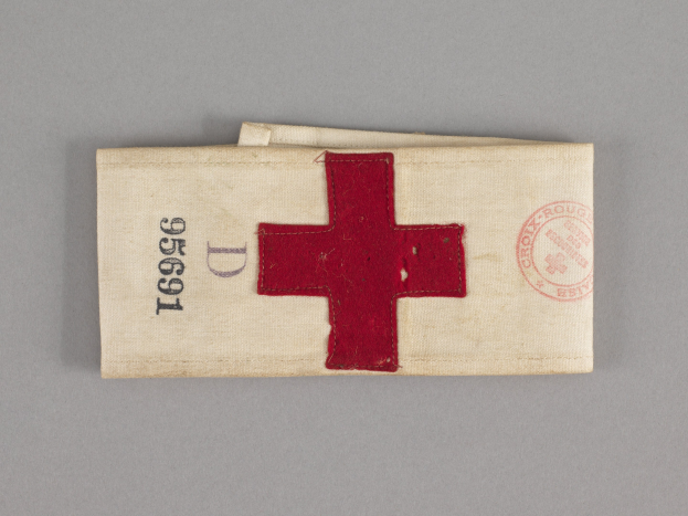 Ein rotes Kreuz-Erste-Hilfe-Set in einem Stoffbeutel mit Text und einem Stempel, das auf einer Oberfläche liegt.