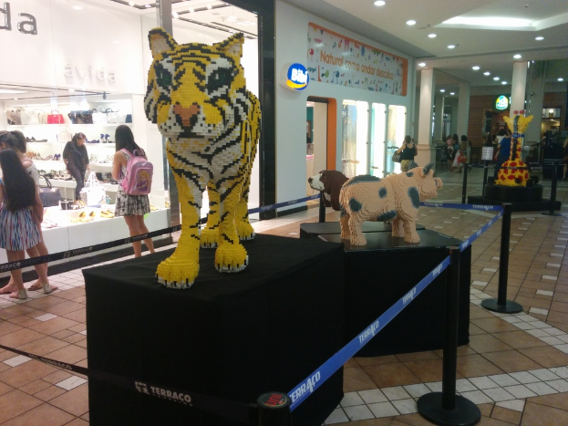 Statuen von Tieren auf schwarzen Kisten umgeben von Stangen mit Gummibändern, mit Geschäften, die Taschen, Schuhe und andere Gegenstände anbieten, und Menschen, die herumlaufen.