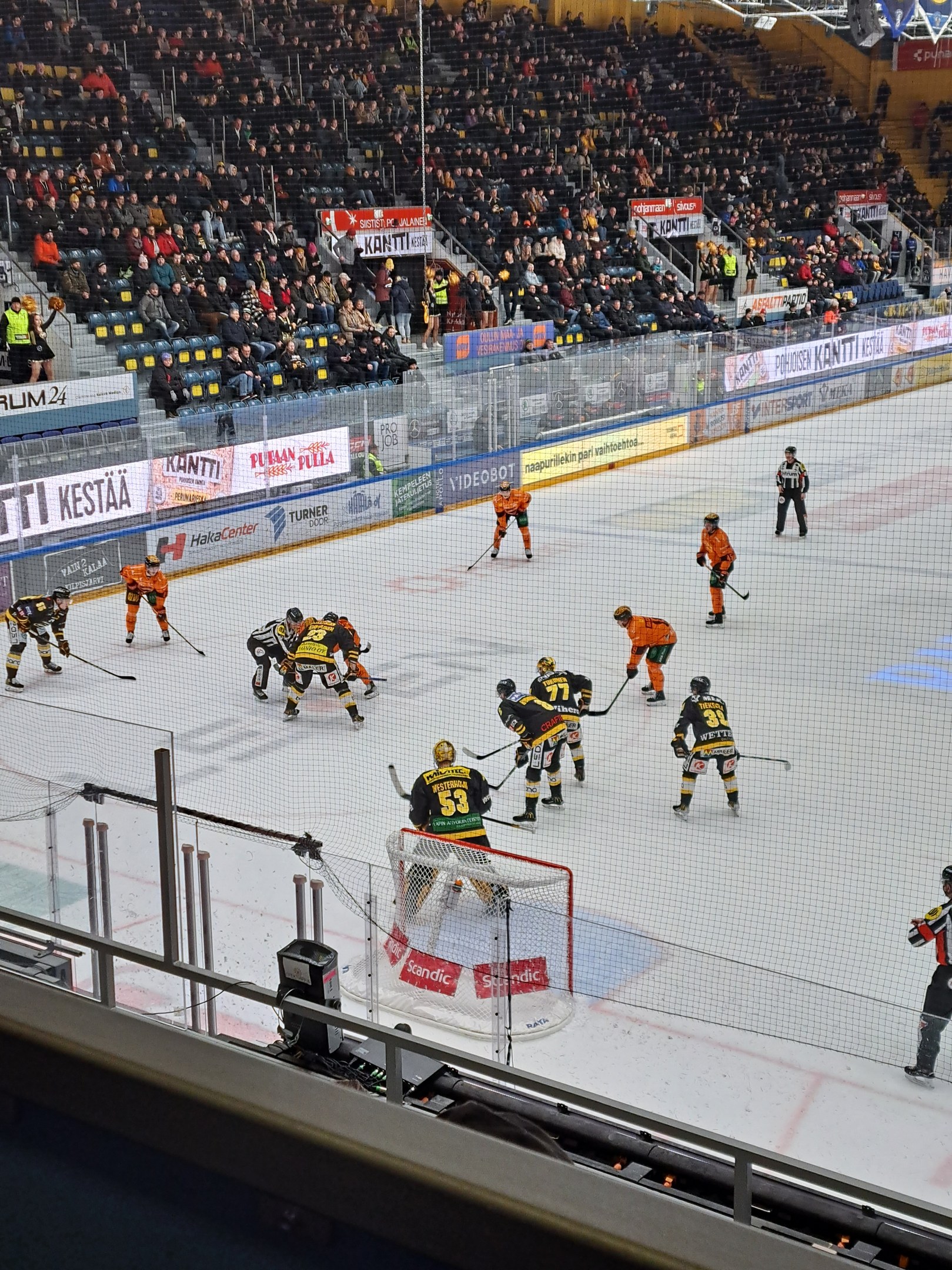 Gruppe von Menschen, die Hockey auf einem Eisstadion spielen, mit Zuschauern, Bannern und Flutlicht überkopf.