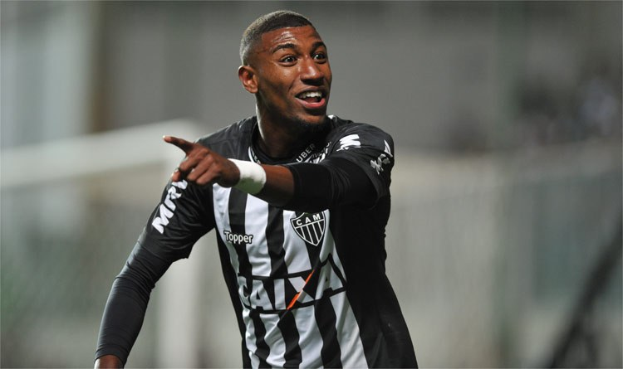 Ein Fußballer in einem schwarz-weißen gestreiften Trikot feiert mit einem Lächeln nach einem Tor, der Hintergrund ist unscharf, um den Moment zu betonen.