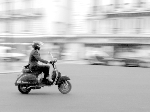 Eine Person, die ein Roller auf einer Stra├če f├Ąhrt.