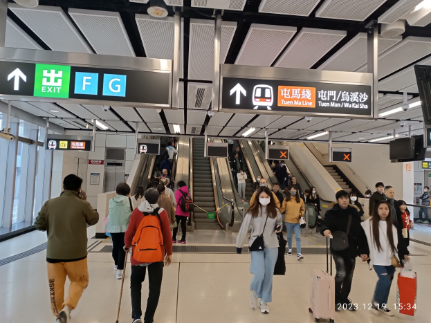 Menschen mit Gepäck durch einen geschlossenen Flughafen gehen, mit Rolltreppen und Informationsanzeigen im Hintergrund.