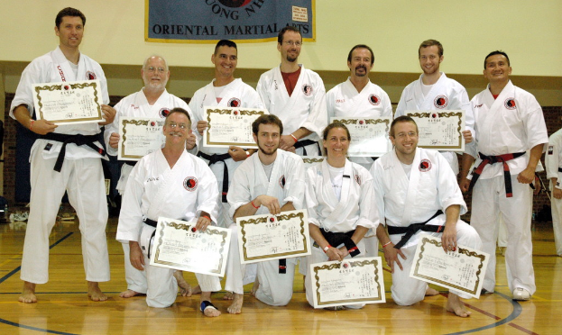 Eine Gruppe von Menschen, die auf dem Boden stehen und sitzen, jeder hält ein Zertifikat, mit einer Werbung im Hintergrund an der Wand.
