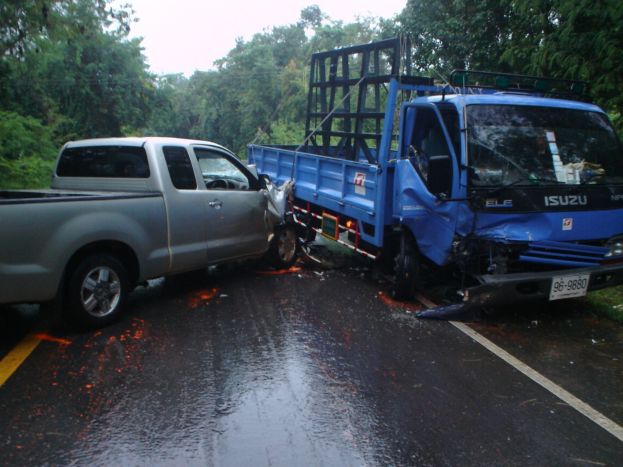 Ein schwerbeschädigter Lkw mit eingedellter Karosserie steht am Straßenrand, umgeben von Bäumen unter einem klaren blauen Himmel.