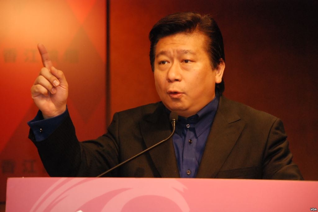 Ein Mann in Anzug und Krawatte, der eine Rede an einem Rednerpult mit Mikrofon hält und ernst dreinschaut.