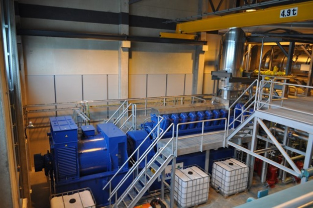 Eine Fabrikinnensicht mit Trögern, Treppe, Gelönder, Containern, Lichtern, Rohren und Wönden.