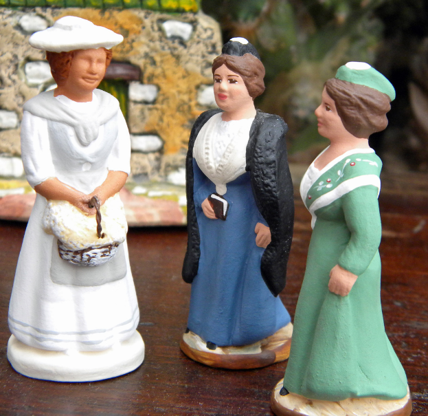 Drei geschnitzte Puppen sind auf einer Holzplatte mit Spielzeughäusern im Hintergrund platziert.