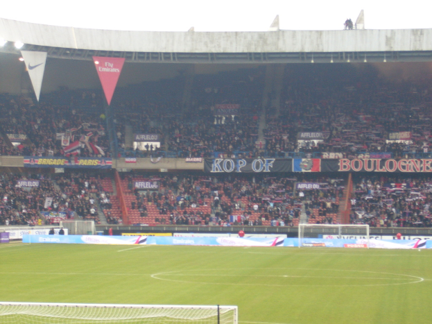 Ein Rasenplatz mit Torpfosten auf beiden Seiten, zahlreichen Zuschauern im Hintergrund und vielen Werbetafeln in der Mitte und darüber.
