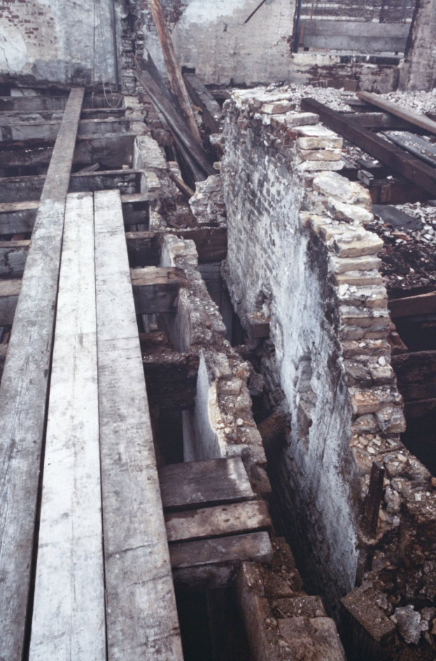 Abriss des alten Gebäudes mit verstreuten Holzplanken und Steinen im Vordergrund und einer remaining Wand im Hintergrund.