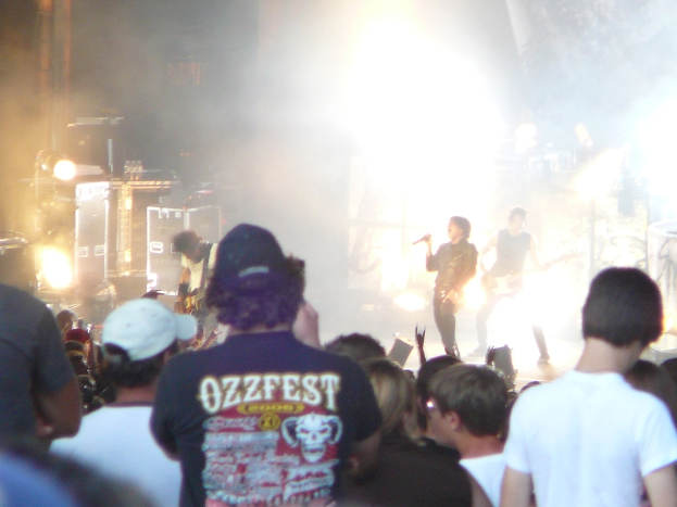 Eine Gruppe von Menschen in verschiedenen Kleidungsstücken, einige mit Mützen, in der Nähe von Musikinstrumenten einschließlich einer Gitarre und einem Mikrofon, mit Bühnenbeleuchtung.