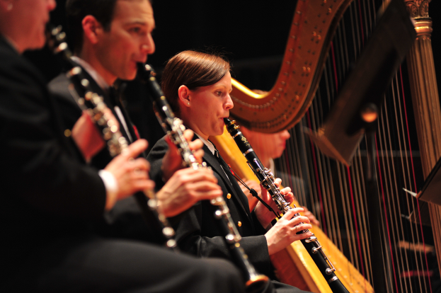 Eine Gruppe von Menschen auf einer Bühne Klarinetten spielend, mit einem Ständer im Vordergrund und einem dunklen Hintergrund.