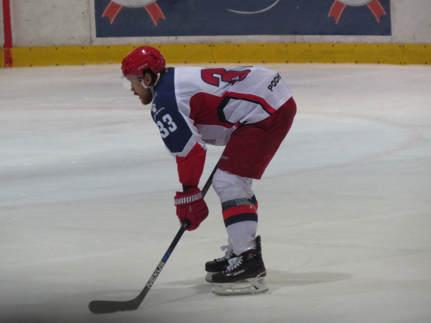 Hockeyspieler in voller Ausrüstung auf dem Eis mit einem Stock, der einer Bannerwand gegenübersteht.