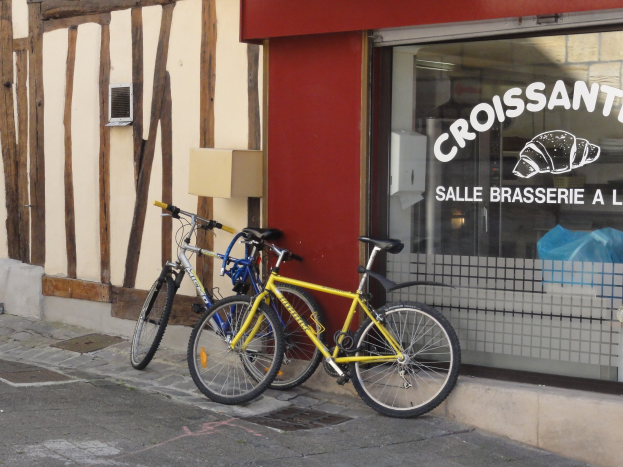 Zwei Fahrr├Ąder nebeneinander auf einem Gehweg vor einem Laden mit einer Glaswand, auf der Text steht und ein Objekt links von den Fahrr├Ądern.