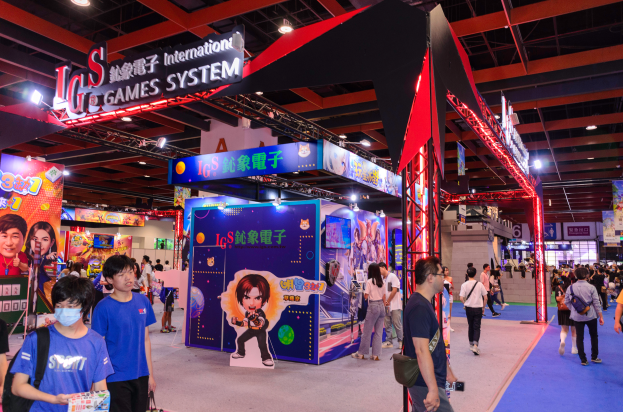 Eine Gruppe von Menschen geht durch eine Messehalle mit Ständen, trägt Taschen und hält Gegenstände, mit vielen anderen im Hintergrund auf einer Spielemesse in China.