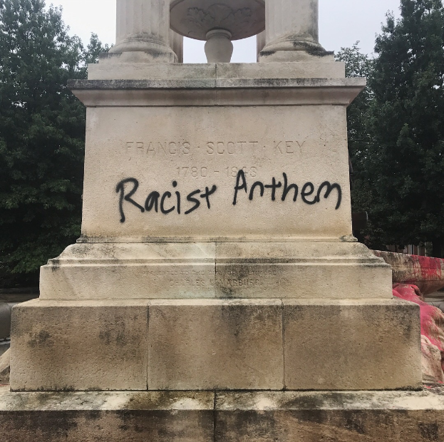 Ein Denkmal mit der Inschrift 'Rassistischer Anthem', umgeben von Bäumen unter einem klaren Himmel.