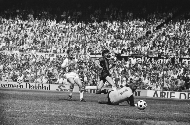 Schwarze und weiße Fotografie von Fussballspielern im Einsatz auf einem Feld mit Zuschauern im Hintergrund und einem Bundesliga 1978-79 Ajax 1-1 Hannover 96-Banner.